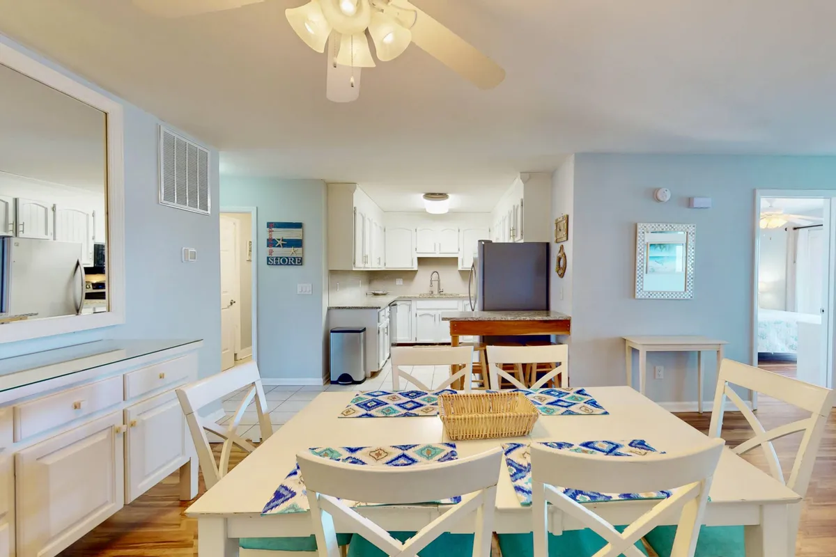 An open-plan interior with a dining table set with a blue-patterned runner positioned adjacent to a kitchen with white cabinetry. The arrangement emphasizes the seamless flow between kitchen and dining areas, ideal for group meals or casual gatherings.