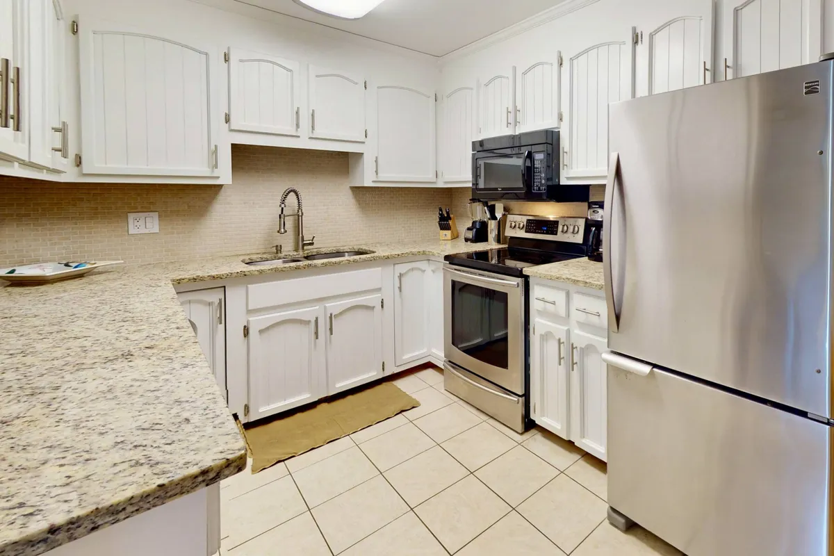 A warmly lit kitchen featuring granite countertops, stainless steel appliances, white cabinetry, and tile flooring. The countertop is spacious, offering ample room for meal preparation, and the overall setup highlights a well-equipped and inviting space for cooking and socializing.